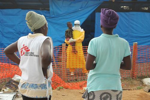 Helena gets a chance to talk to her son Moses who is an Ebola confirmed patient. A MSF health promoter supports this difficult moment for the young mother as she is too overwhelmed with what to say. The health promoter advises her to say positive things such as „I am waiting here outside for you“ or „I am thinking of you non Stop“