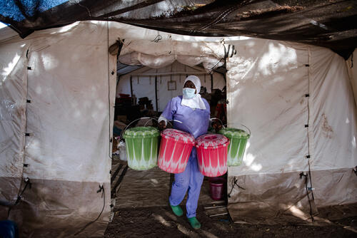 Cisse, a health promoter, carries buckets with kits given to every patient who comes to receive treatment for diphtheria from the logistics tent set up on the ground of the Centre de Traitement Epidemiologique to the waiting area where patients are at the center in Siguiri, Guinea. The kit was made to allow them to spend five days there and to easily clean and dispose of it, as necessary. MSF has helped treat over 2100 patients as of Jan. 4, 2024, and has been responding to a diphtheria outbreak in the region since mid-August, the likes of which has not been seen in the country for the last 30 years.
