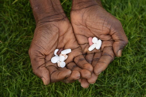 Image of medicine for the treatment of drug resistant tuberculosis (DR-TB). The left hand contains pills from the recently approved BPaLM 6-month shorter regimen treatment and the right hand contains pills from the longer 18 months regimen treatment. Following the validation of shorter regimen by WHO, MSF started supporting the Ministry of Health in implementing shorter regimen for patients affected by DR-TB since 2022 in Sierra Leone. Depending on individual patients’ diagnostic and clinical situation treatment regimens are initiated. Shorter regimens are often preferred by patients and medical professionals as longer treatment can be physically and mentally harder to adhere to.