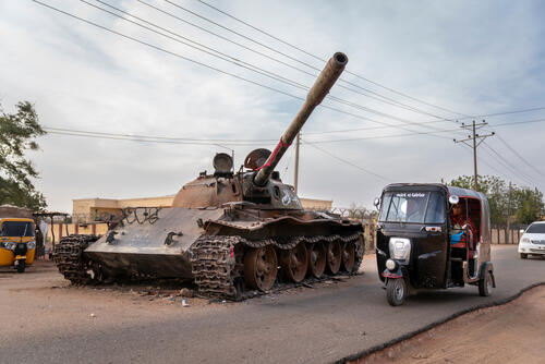 A rickshaw taxi goes around a destroyed tank belonging to the Sudanese Armed Forces, a remnant of the violent clashes that took place in El Geneina in 2023. West Darfur, Sudan. February 20, 2024. Copyright Diana Zeyneb Alhindawi