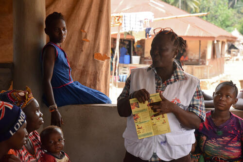 MSF health promoter, Beatrice Turay, standing in front of community members in Rogbereka village, Tonkolili district, holding a vaccination card for children under the age of five and discussing about the importance of vaccination, the various vaccines available for children and how mothers and caregivers can access them.