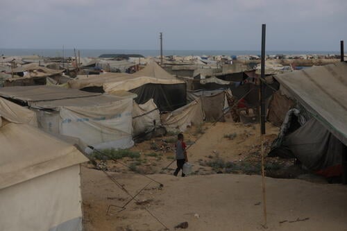 A young boy carries a water jerrycan through the Mawasi Khan Younis displacement tents, where patched and worn-out tents offer little shelter. Israel's ban on fishing and swimming increased the desperate need for fresh water for displaced Palestinians in Gaza.