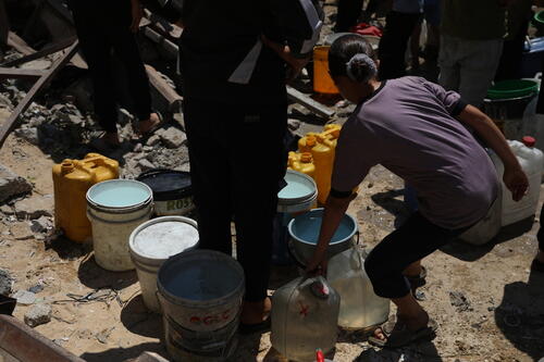 Palestinians wait with worn-out containers to fill them from a truck. The scarcity of water and the danger of collection create immense tension.