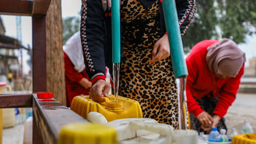 Open water taps fed by an NGO-supported large red tank, with women filling water gallons in the Ghweiran neighborhood of Hasakah, northeast Syria.