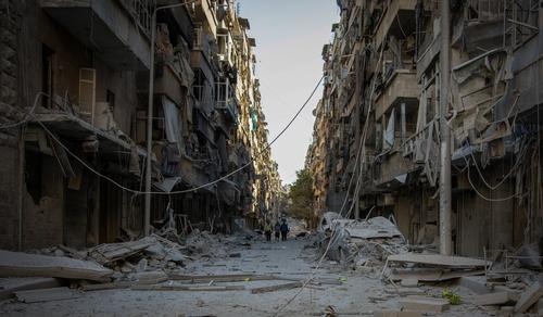 People walk down a street in Bustan Al Kasr neighbourhood after it was hit by airstrikes in mid-October 2016.