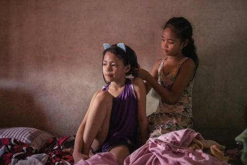 Young girls Elyes and Diana fix each other's hair before posing for a portrait in their tenement home near Smokey Mountain, Manila. Both girls are recipients of free vaccinations from Likhaan clinic, which provides free healthcare for low income communities.
