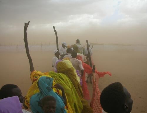 Darfur, Kalma Camp, 2007. During the rainy season there are frequent sand storms (haboob). On occasion, the wall of sand is so thick; it is dark despite of the time of day. However, the weather did not interrupt the distribution line in this photograph.