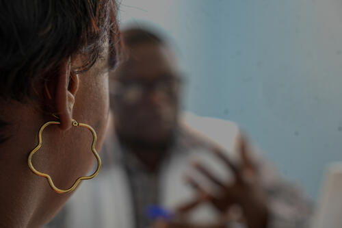 In the foreground, a 27-year-old survivor, mother of two – a six-year-old boy and an eight-month-old baby – confides in a member of MSF staff. After her husband was killed in an armed attack in their neighbourhood, she was subjected to sexual violence. She then fled with her children to a displacement camp.