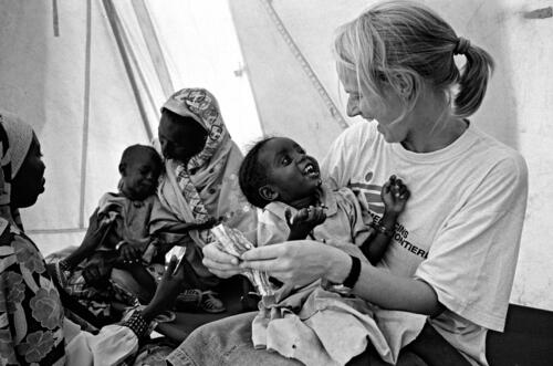 Tova, swedish nurse working for MSF-B, is holding Fatne Abakar, 3 years old, on her knees to distract her. Behind her, Tova's assistent, is helping a mother to feed her child with the food given in the feeding center.When Fatne arrived in the camps of Iridimi, she was severely malnourished. Now, she gained a little weight and soon wil be able to leave the therapeutic feeding center's daily programme.Tova,Une infirmière suédoise de MSF-B tient Fatne Abakar, 3 ans, sur ses genoux pour la distraire. Derrière, une mère, aidée d'une assistante tchadienne de Tova, tentent de calmer un enfant qui refuse de manger ce que le centre nutritionnel prévoit comme alimentation  dans leur prg.A l'arrivée au camps de Iridimi, Fatne était sévèrement sous-alimentée. Aujourd hui elle a repris du poids et pourra bientôt quitter le prg quotidien du Centre Nutritionnel Thérapeutique de MSF-B.