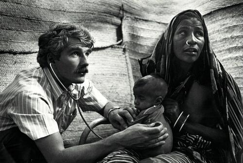 Le Dr. Francis Charhon examine l'enfant d'une jeune femme au Faw camp. Quelques 600.000 Ethiopiens fuyant la sécheresse, la famine et les combats dans leur pays ont trouve refuge au Soudan. Quittant la province de Tigray (Ethiopie) qui réclame l'indépendance et ou il n'y a plus aucun moyen de subsistance, et pris en charge par le TPLF (Front de Libération Tigrayen), les réfugiés parcourent ainsi des centaines des kilomètres a pied ou en camion. Pendant le voyage, leur nourriture est tant bien que mal assurée par le TPLF. A leur arrivée au Soudan, ils sont accueillis dans deux camps situes dans l'est du pays : celui de Tekaloubab - ou Tukulubab (Kassala) - et celui plus au sud de Wad Khouli, appelé à devenir le plus grand des centres de réfugiés ; les réfugiés seront ensuite transférés 350 km plus loin, dans les camps Fau 1, 2 et 3. Leur subsistance est tributaire de l'acheminement en nourriture et en eau, irrégulier et insuffisant. Leur santé, surveillée et assurée par le HCR, pendant le voyage se dégrade très rapidement et nombreuses sont les épidémies de rougeole et de tuberculose.